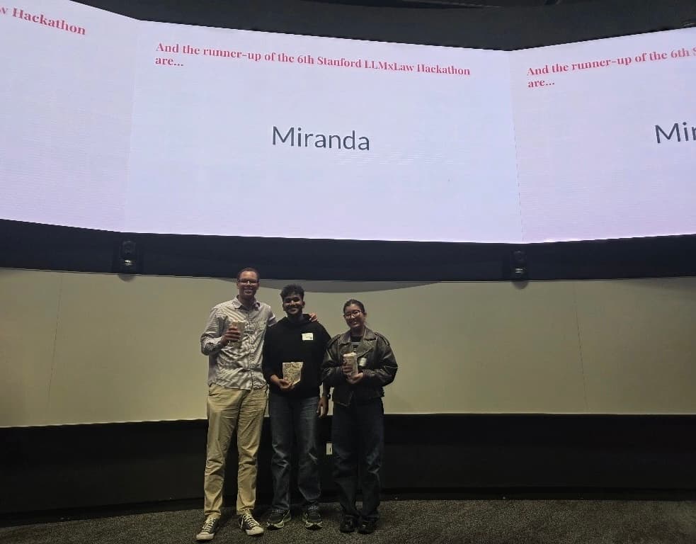 Emma with teammates on stage at Stanford LLMxLaw Hackathon, runner-up announcement on screen behind them